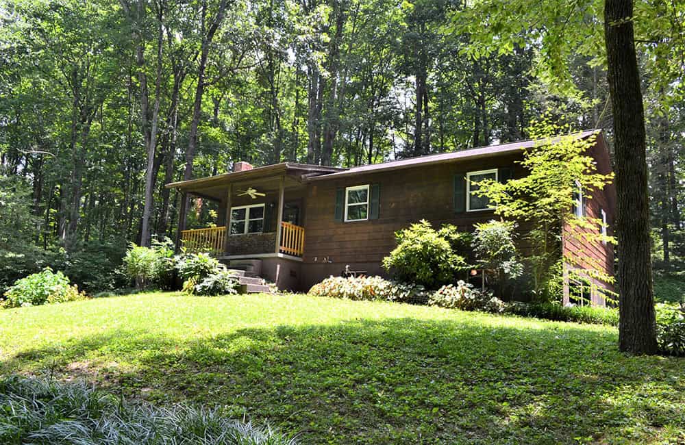 a house with a porch and a lawn in the woods